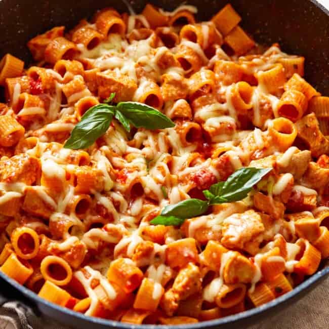 a skillet full of pasta with chicken and basil.