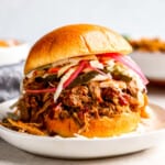 a pulled pork sandwich with coleslaw on a white plate.