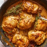 chicken breasts in a skillet with sauce and sprigs of thyme.