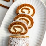 a slice of pumpkin roll with powdered sugar on a white plate.