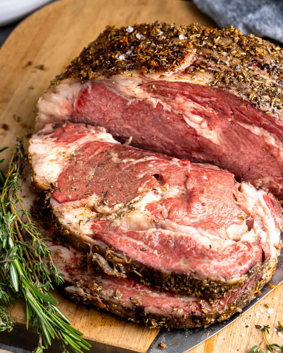 a prime rib roast with herbs on a cutting board.