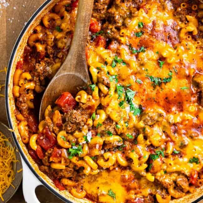 cheesy goulash in a pan with a wooden spoon.