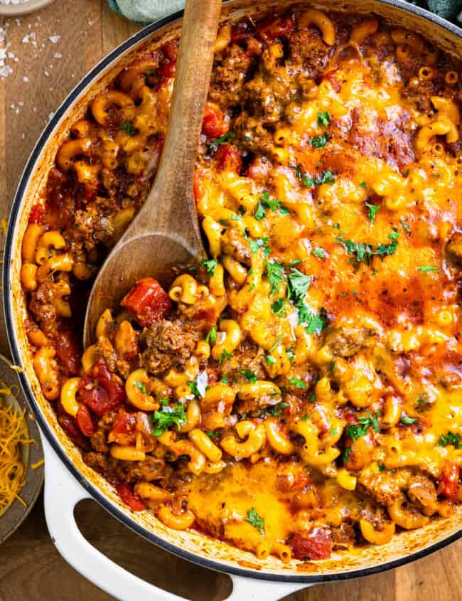 cheesy goulash in a pan with a wooden spoon.