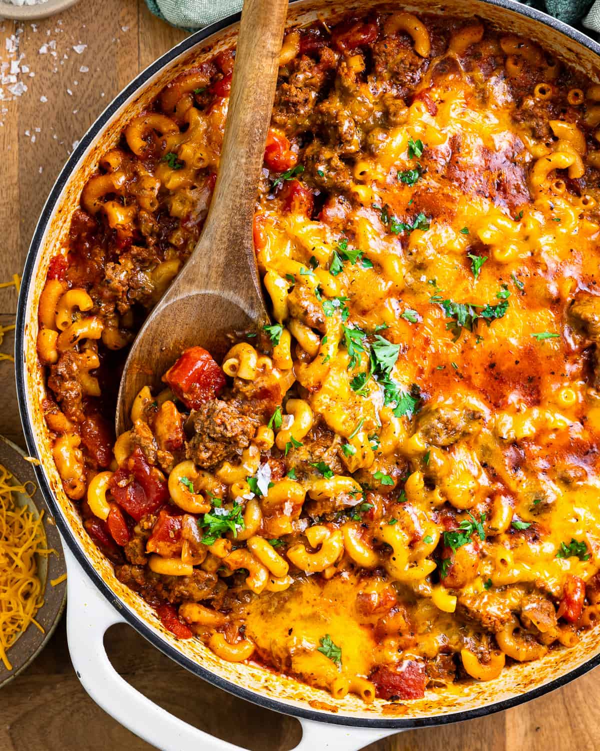 cheesy goulash in a pan with a wooden spoon.