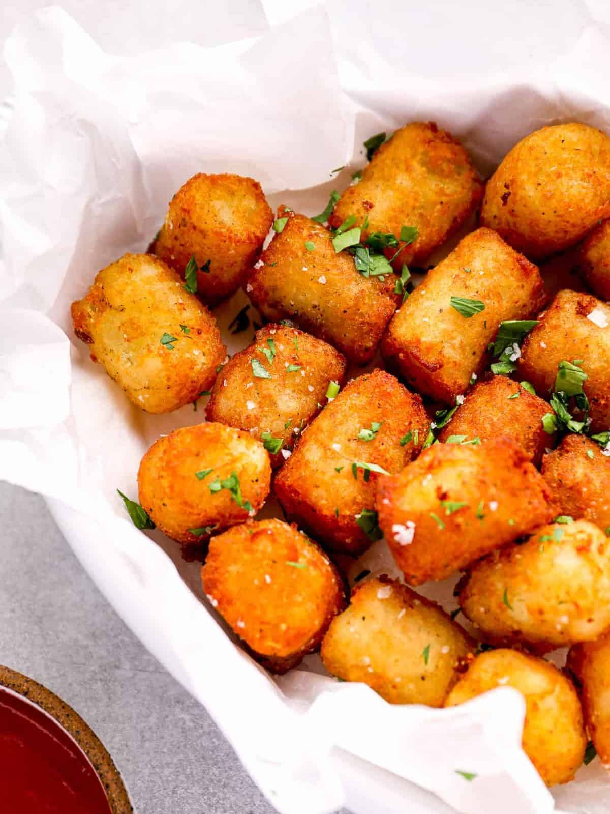 three-quarters view of homemade tater tots in a parchment-lined serving dish topped with parsley.