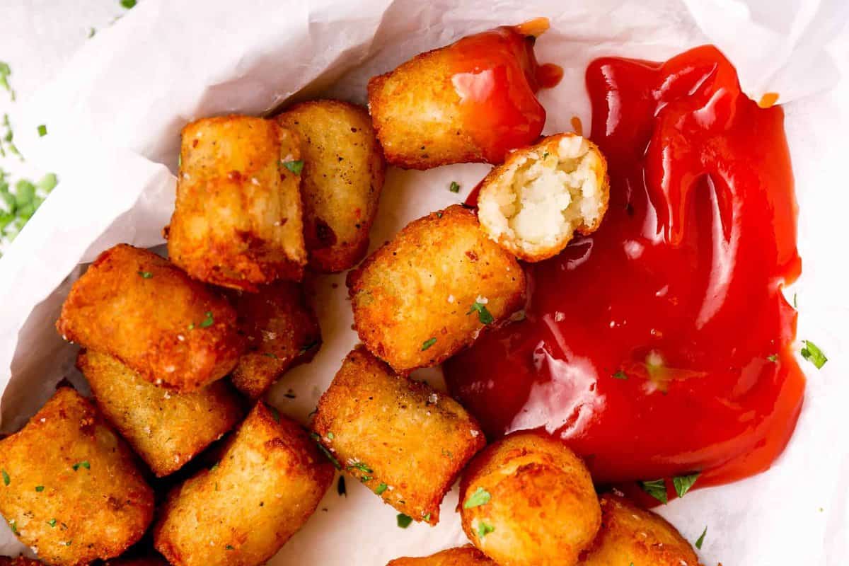 overhead view of crispy tater tots in a parchment-lined serving dish with ketchup.