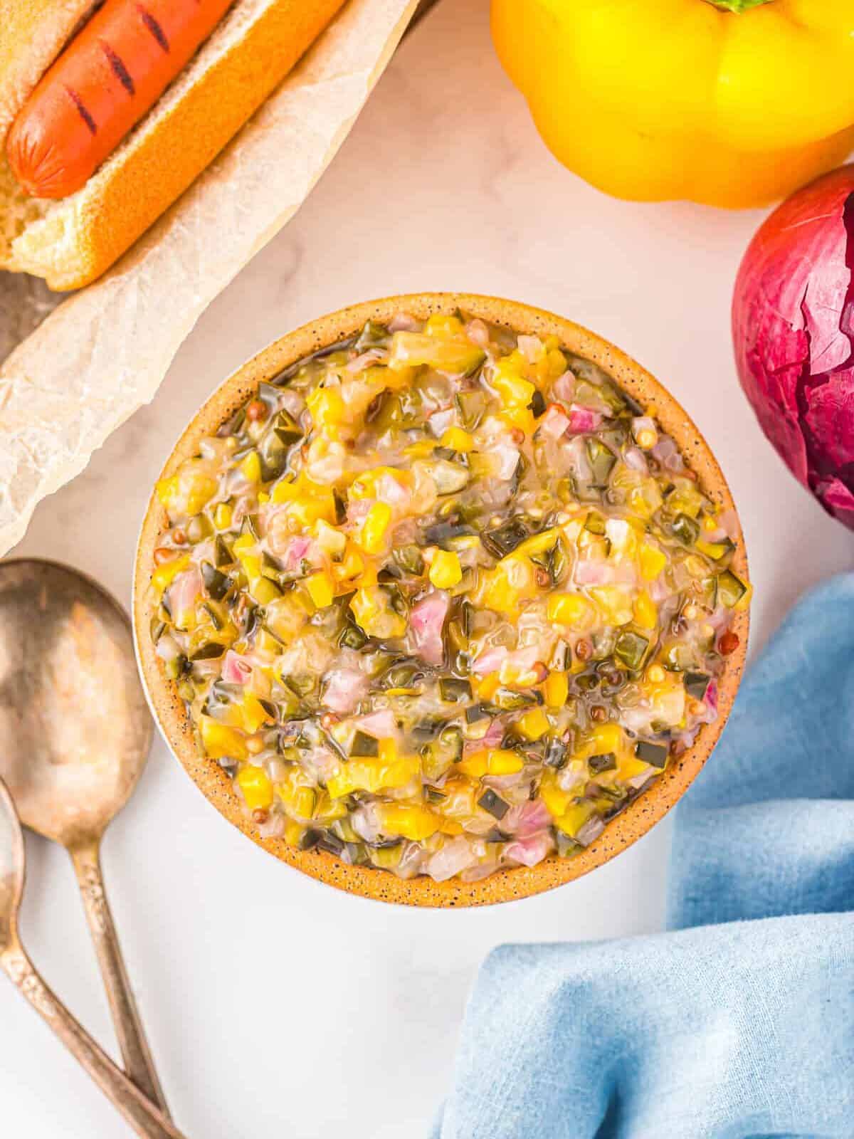 overhead view of sweet pickle relish with cucumbers, red onions, and bell peppers, in a white bowl.