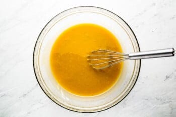 a bowl of orange sauce with a whisk in it.