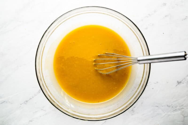 a bowl of orange sauce with a whisk in it.