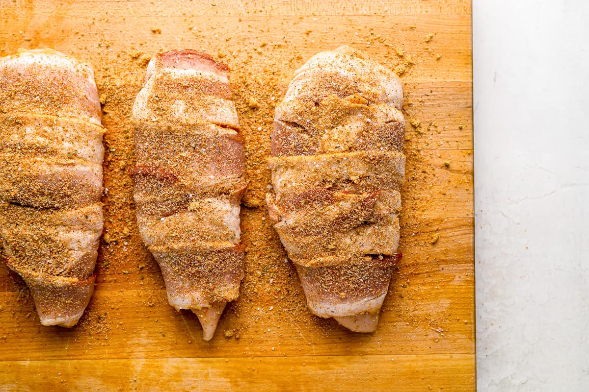 three pieces of bacon wrapped chicken on a cutting board.