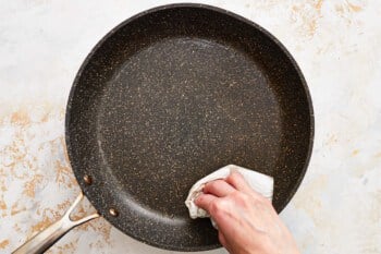 a person wiping a frying pan with a cloth.