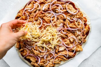 a person putting cheese on a pizza.