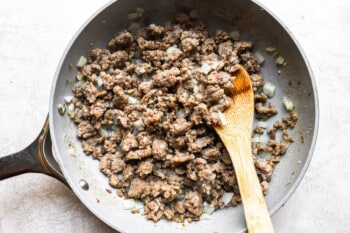 ground beef in a frying pan with a wooden spoon.