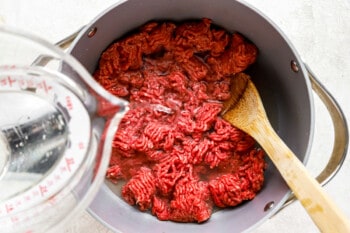a bowl of ground beef in a pan with a wooden spoon.