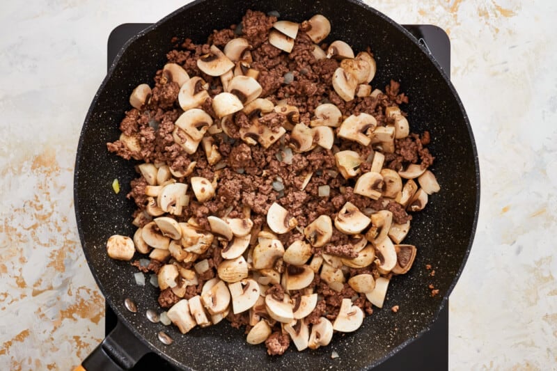 a frying pan with ground beef and mushrooms.