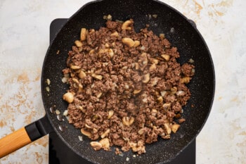 a frying pan with ground beef and cashews.