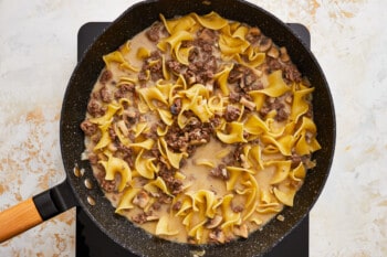 a skillet with noodles and meat in it.