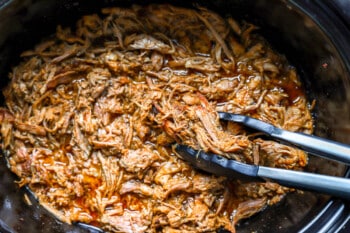 pulled pork in a slow cooker with two forks.
