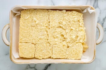 a white baking dish with squares of bread in it.