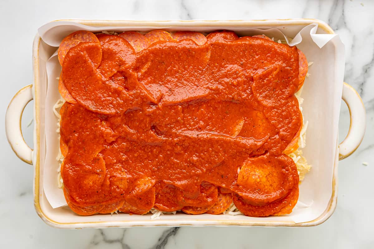 Slider rolls topped with tomato sauce in a baking dish. 