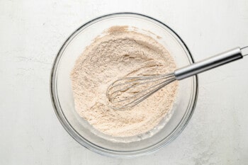 a bowl of flour with a whisk in it.