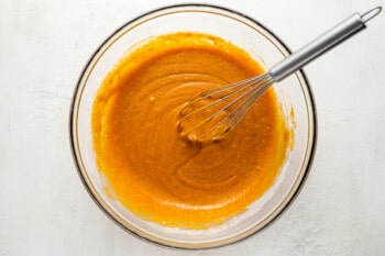 a bowl of orange batter with a whisk in it.