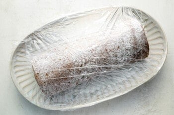 a cinnamon roll wrapped in plastic on a plate.
