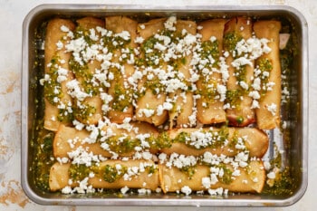 stuffed enchiladas in a baking dish with feta cheese and pesto.