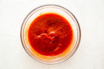red sauce in a bowl on a white surface.
