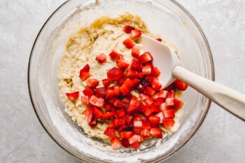 a bowl of dough with strawberries and a spatula.
