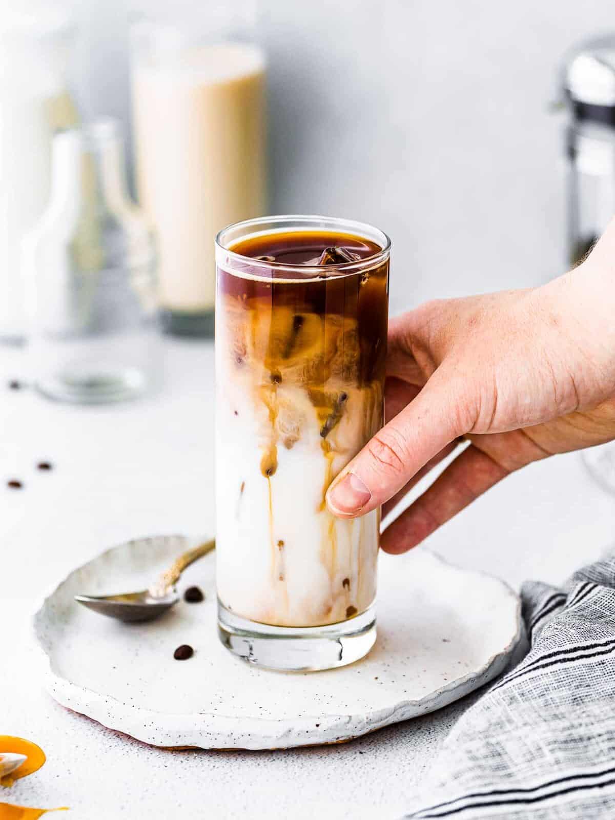 hand holding iced caramel macchiato in tall glass