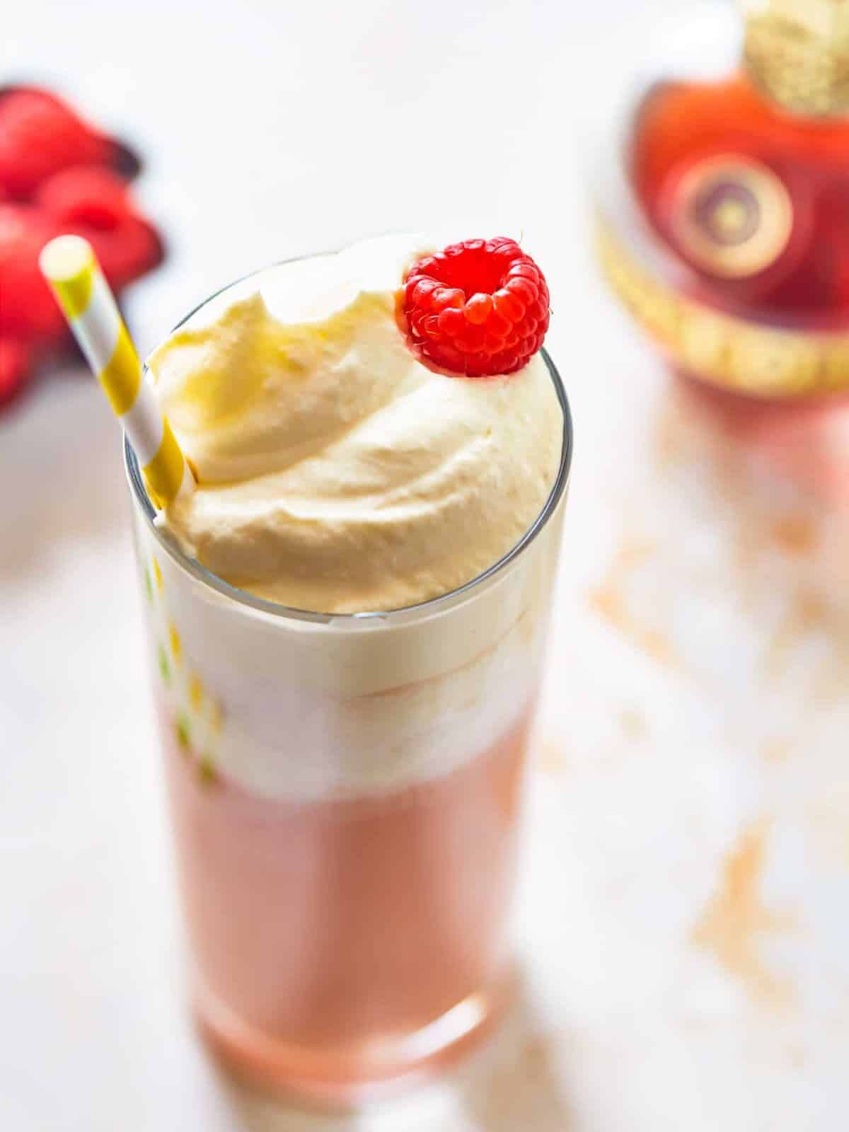 three-quarters view of raspberry italian cream soda in a tall glass topped with whipped cream, a raspberry, and a straw.