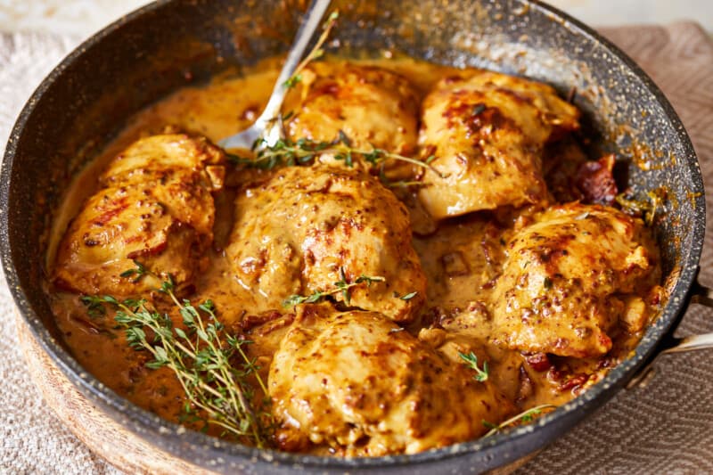 chicken thighs in a pan with sauce and sprigs of thyme.