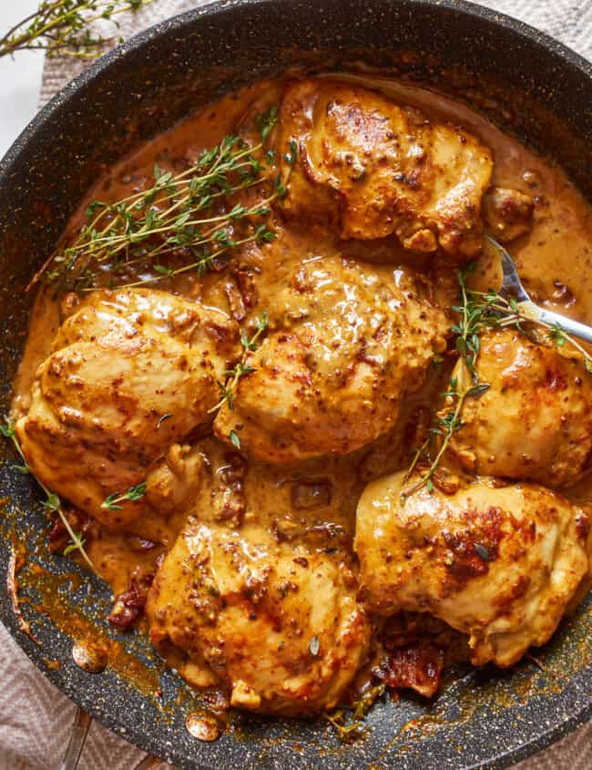 chicken breasts in a pan with sauce and sprigs of thyme.