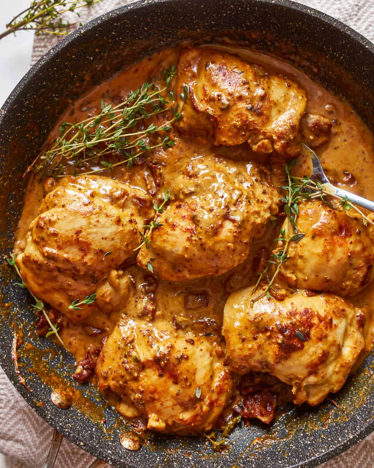 chicken breasts in a pan with sauce and sprigs of thyme.