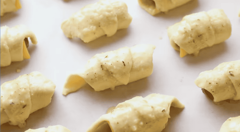 seasoning brushed onto pigs in a blanket on a baking sheet.