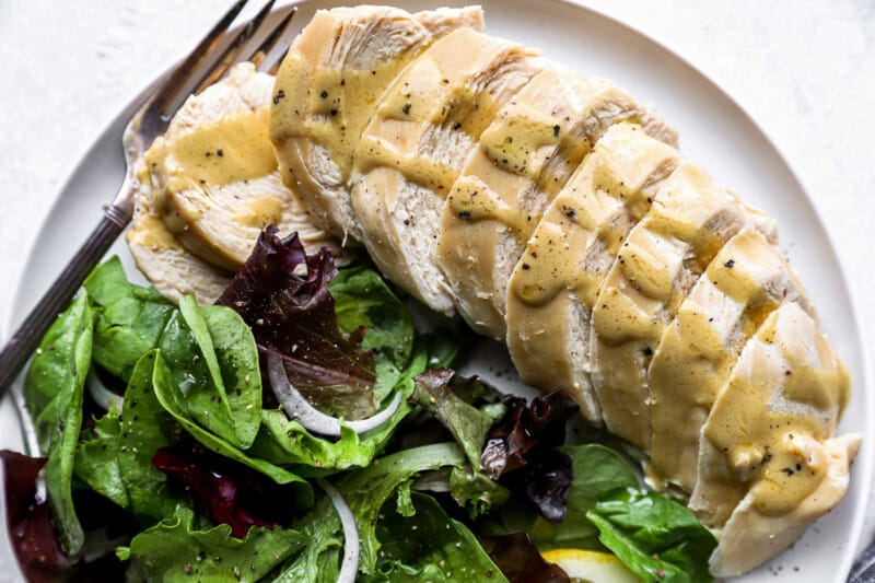 partial overhead view of a sliced poached chicken breast on a white plate with greens and a fork.