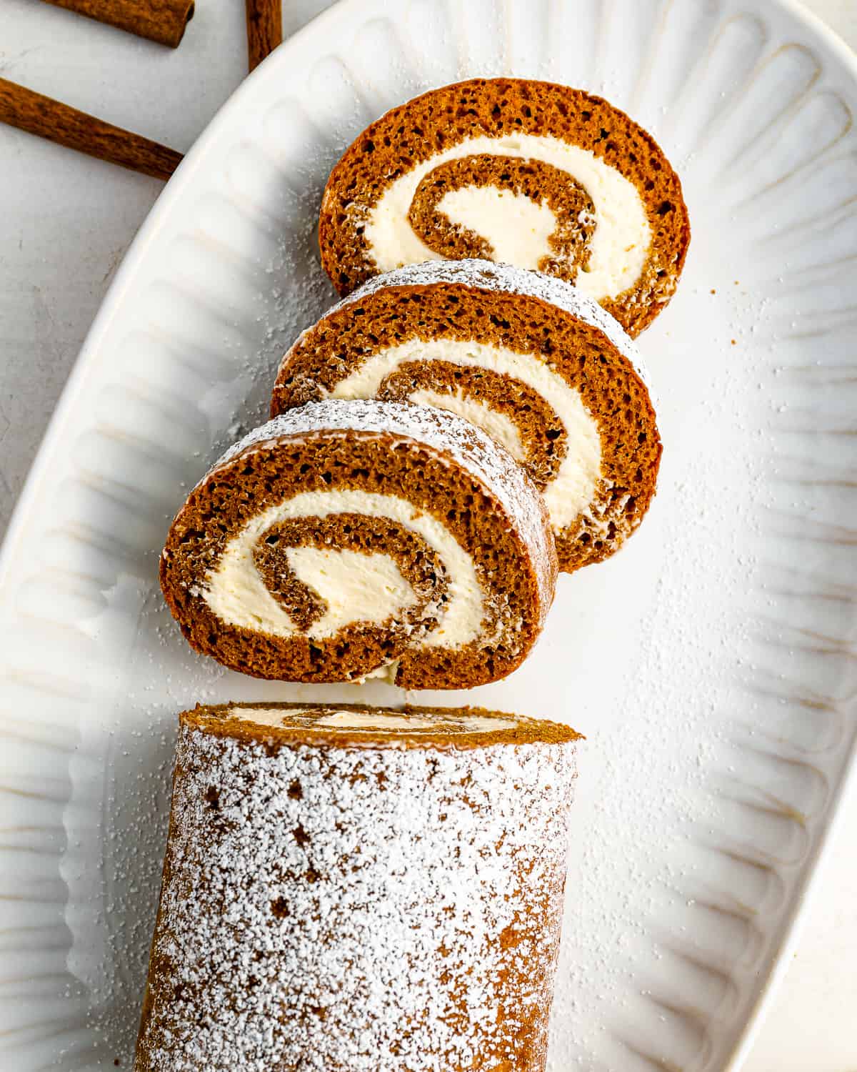 sliced of pumpkin roll cake filled with cream cheese, on a serving plate.