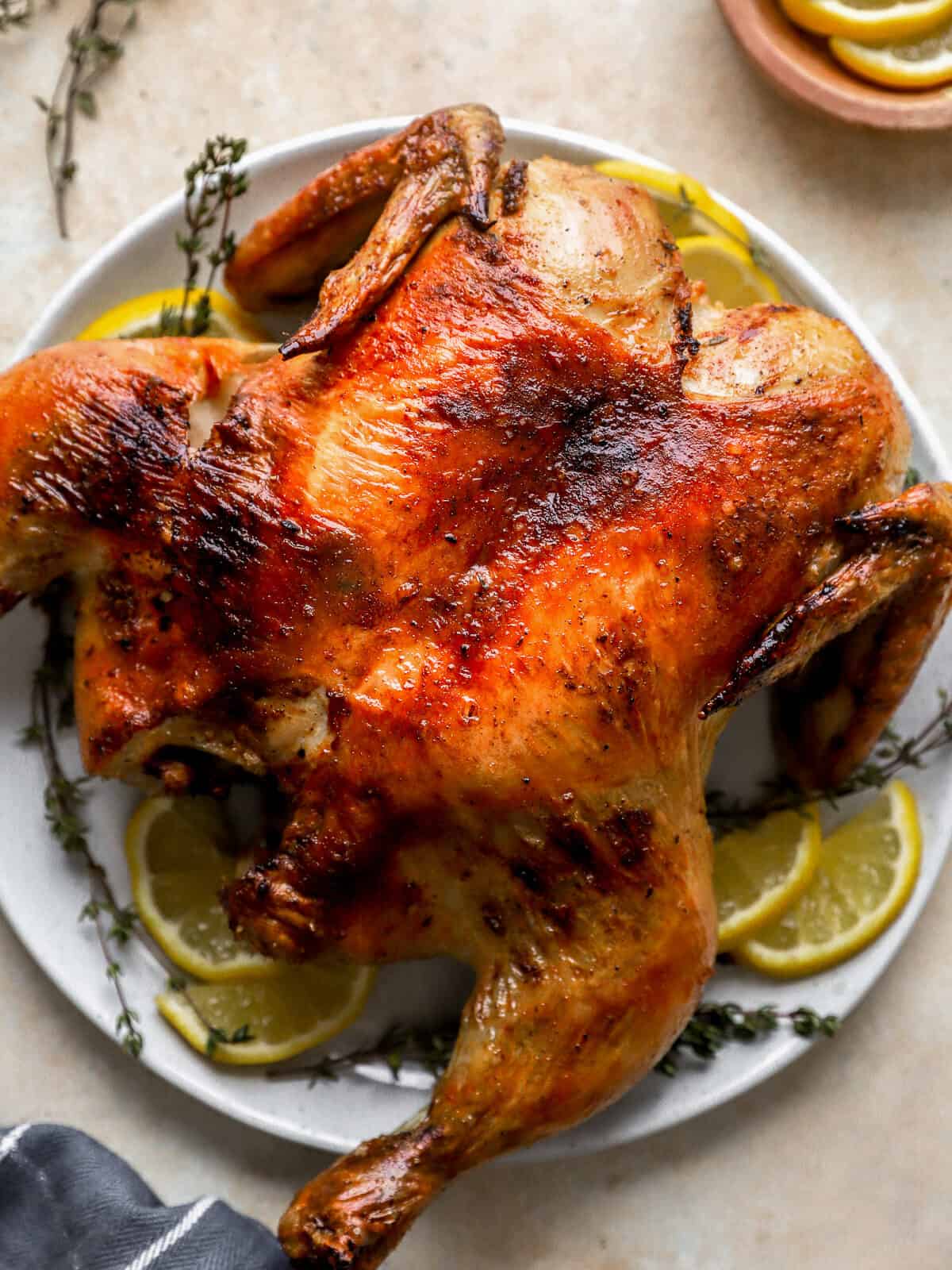 spatchcock chicken on a white plate with lemon slices.