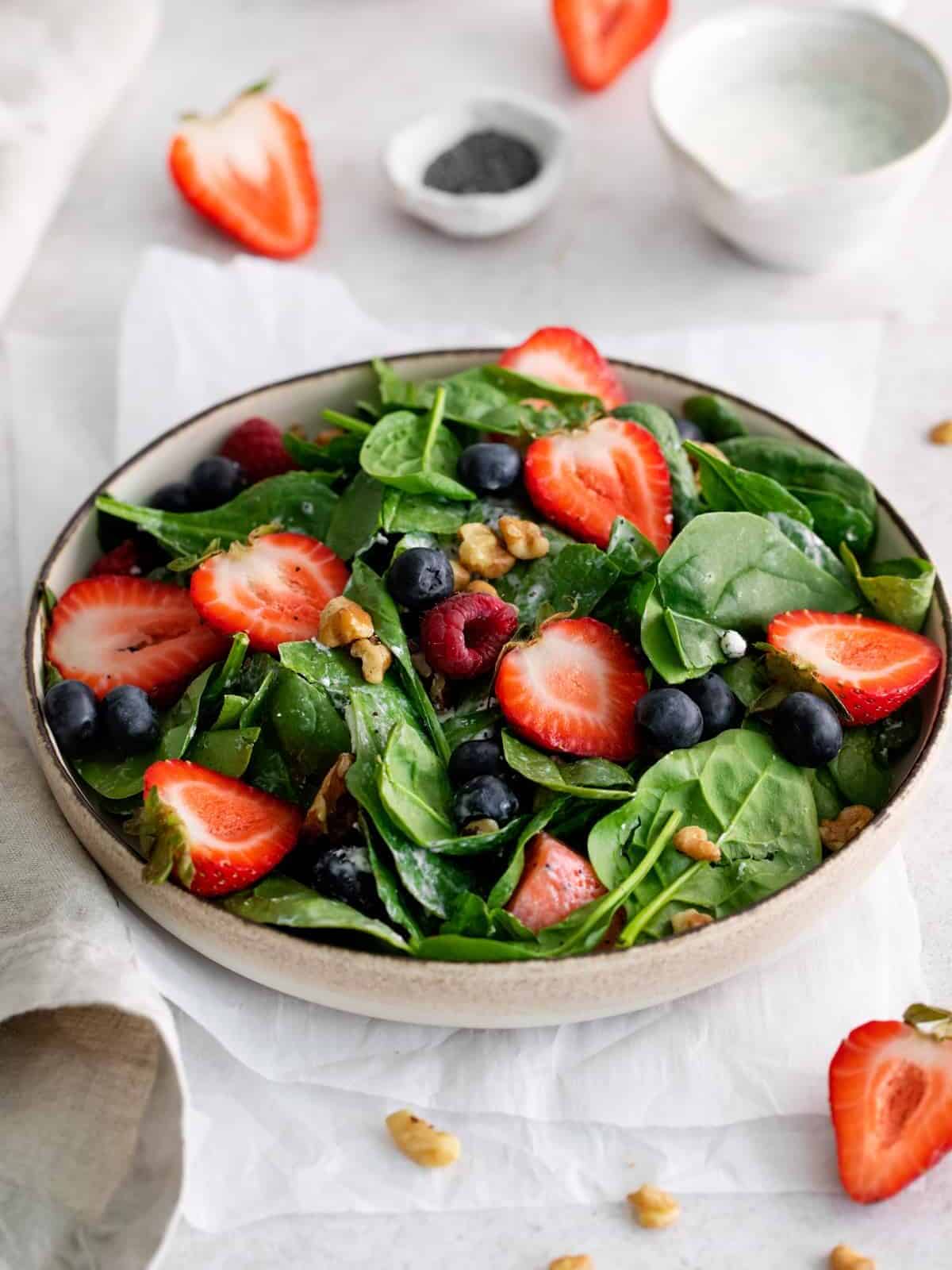 three-quarters view of spinach salad with mixed berries in a beige bowl.