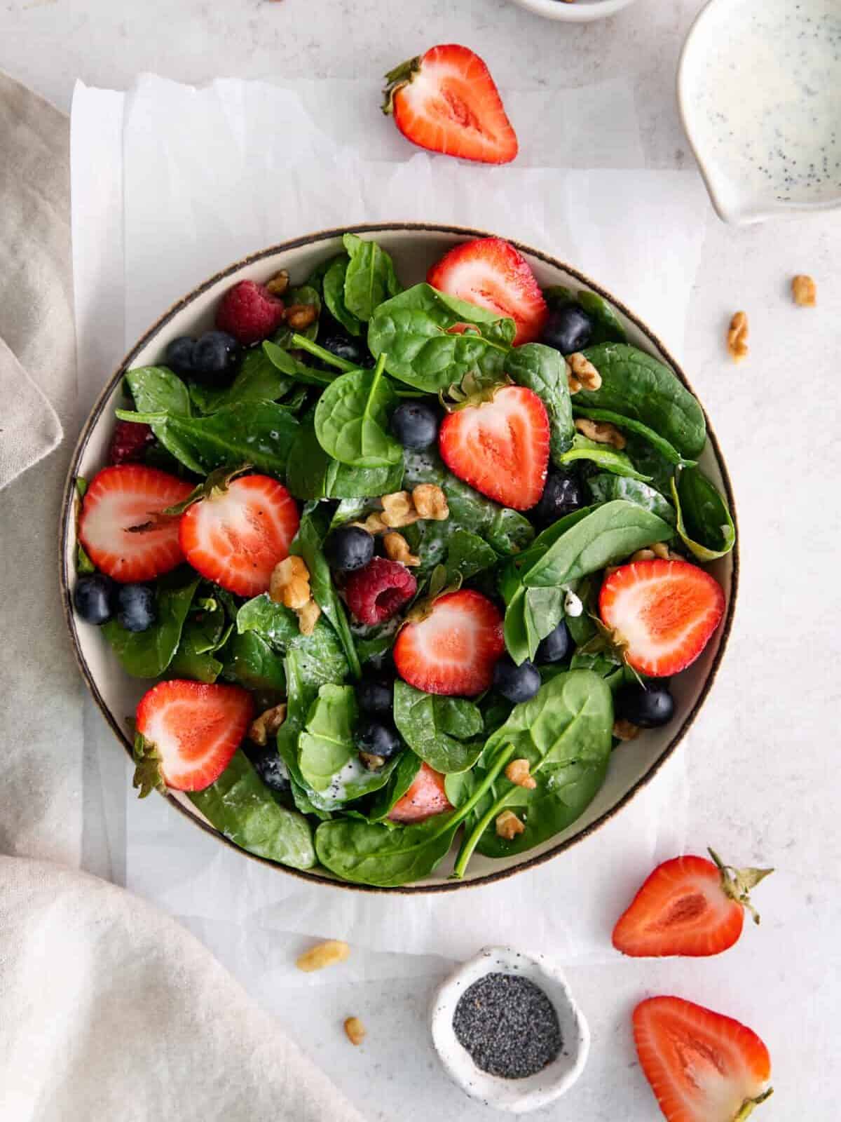overhead view of spinach berry salad in a beige bowl.