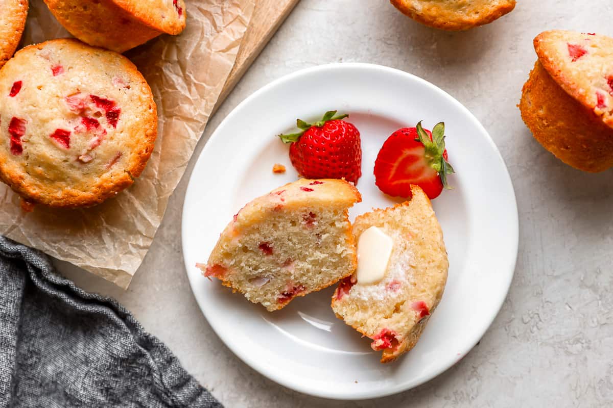 strawberry muffin cut in half with a pat of butter, sitting on a white plate with strawberries.