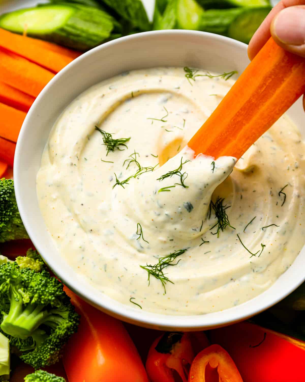 a person is dipping a carrot stick into a bowl of vegetable dip.