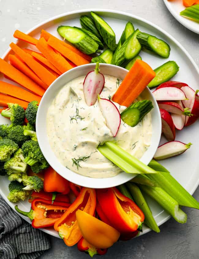 a plate of dip with vegetables and radishes.