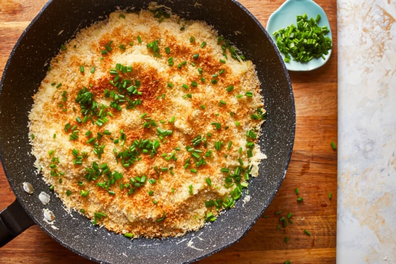 a frying pan with cheese and parsley on a wooden table.