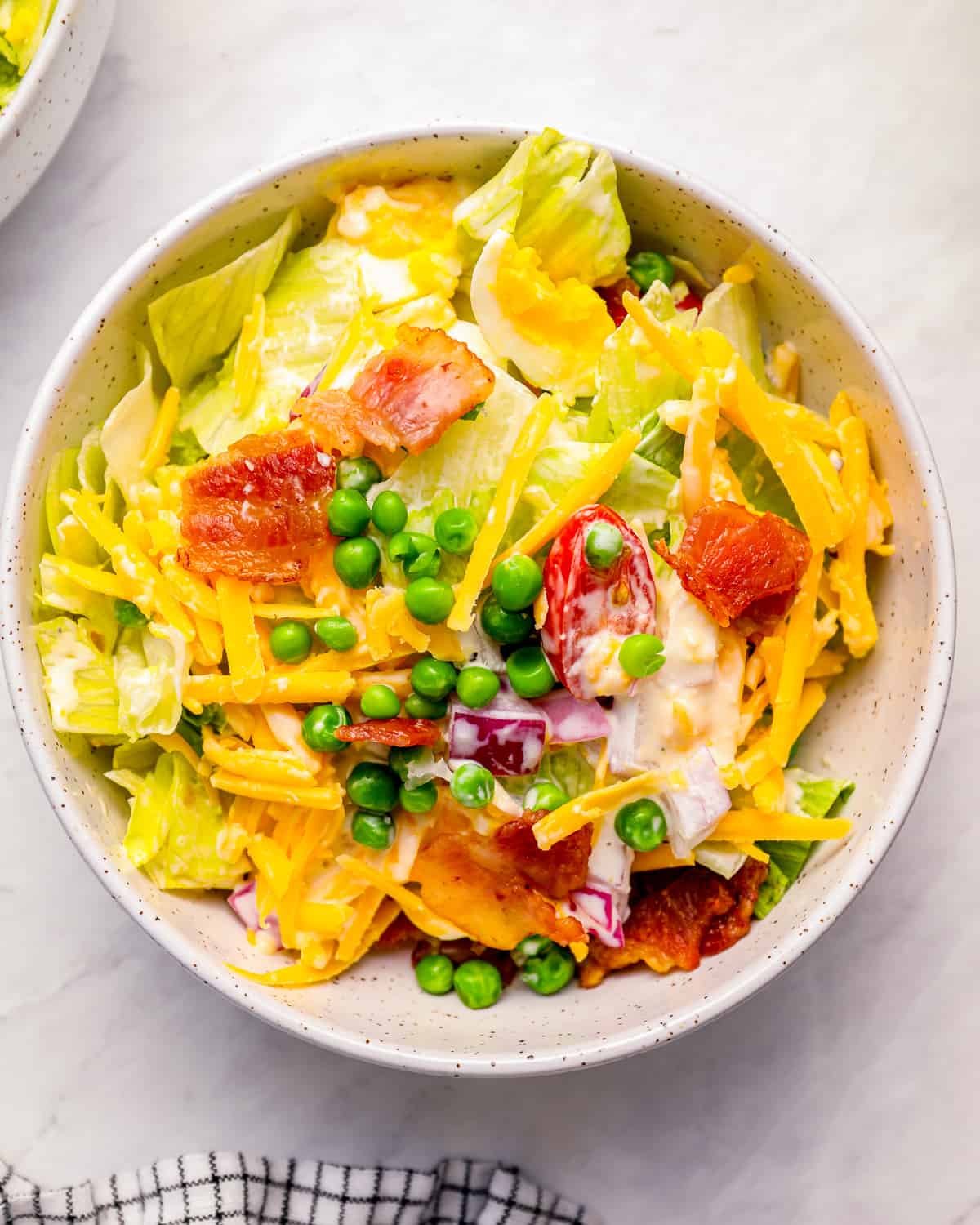 A bowl of 7 layer salad with bacon and peas.