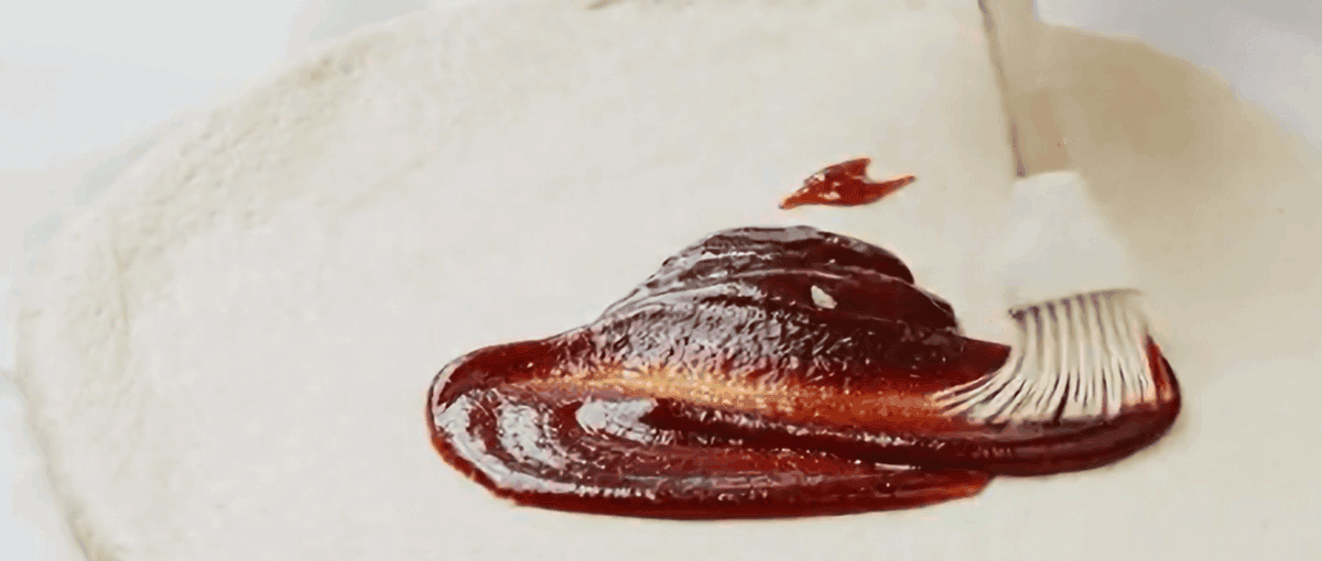 Spreading bbq sauce over pizza dough.