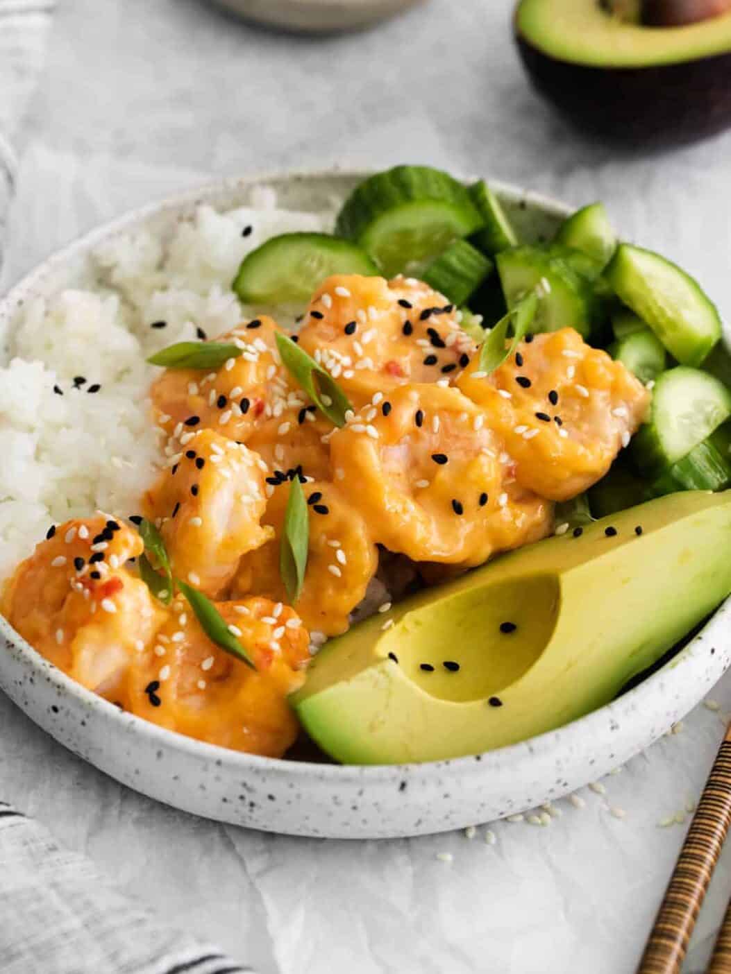three-quarters view of a bang bang shrimp bowl with with sushi rice, cucumbers, and avocado.