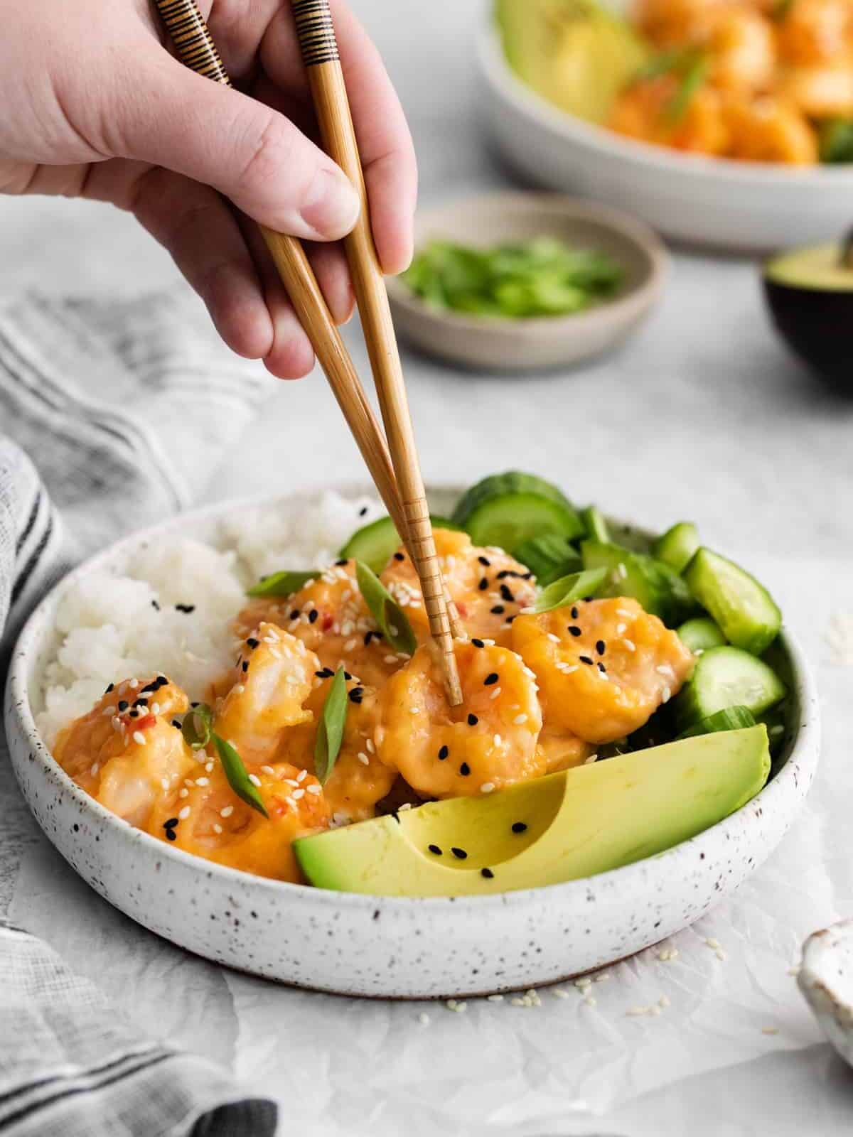 a hand using chopsticks to grab a shrimp from a sushi rice bowl.