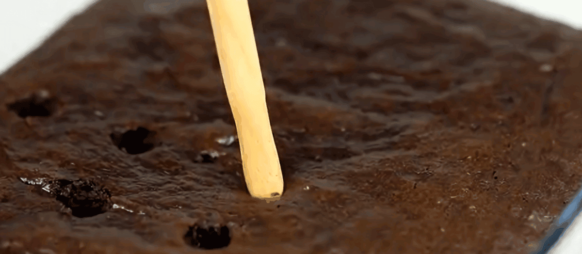 Poking holes in a chocolate cake.